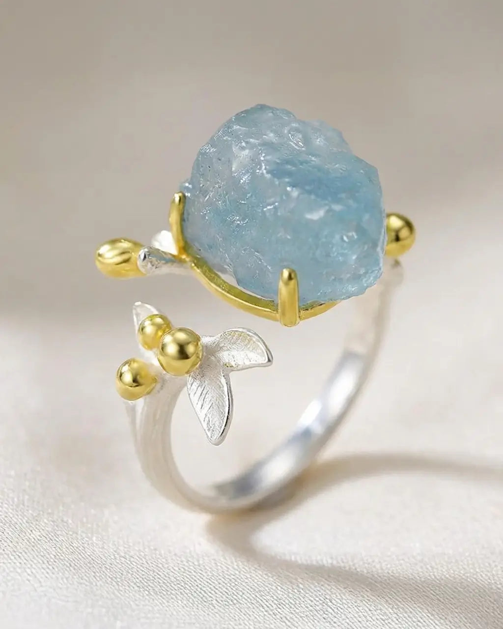 Bague de l’Eau en argent 925 avec aquamarine brute posée sur fond clair, mettant en valeur la pierre naturelle et les détails dorés.