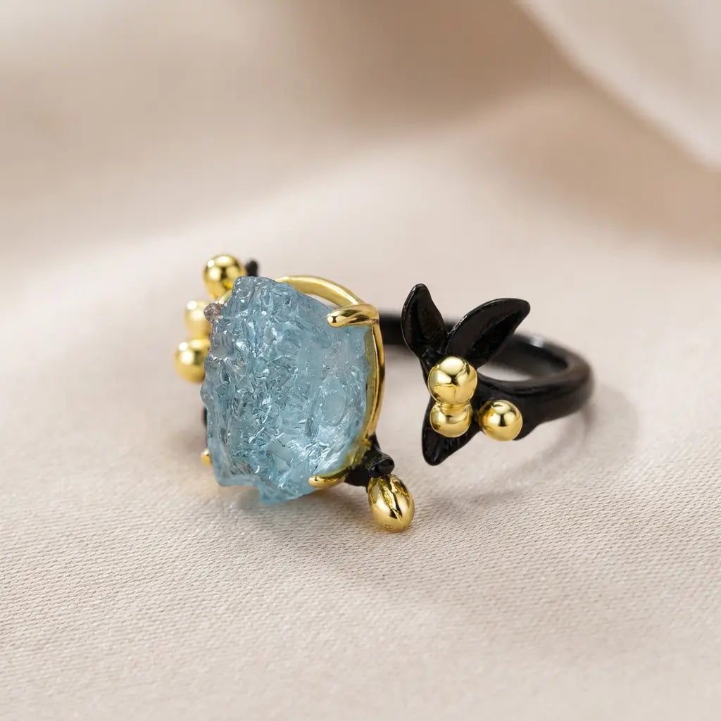 Bague version noire en argent 925 avec aquamarine brute posée sur textile clair, ambiance douce et élégante.