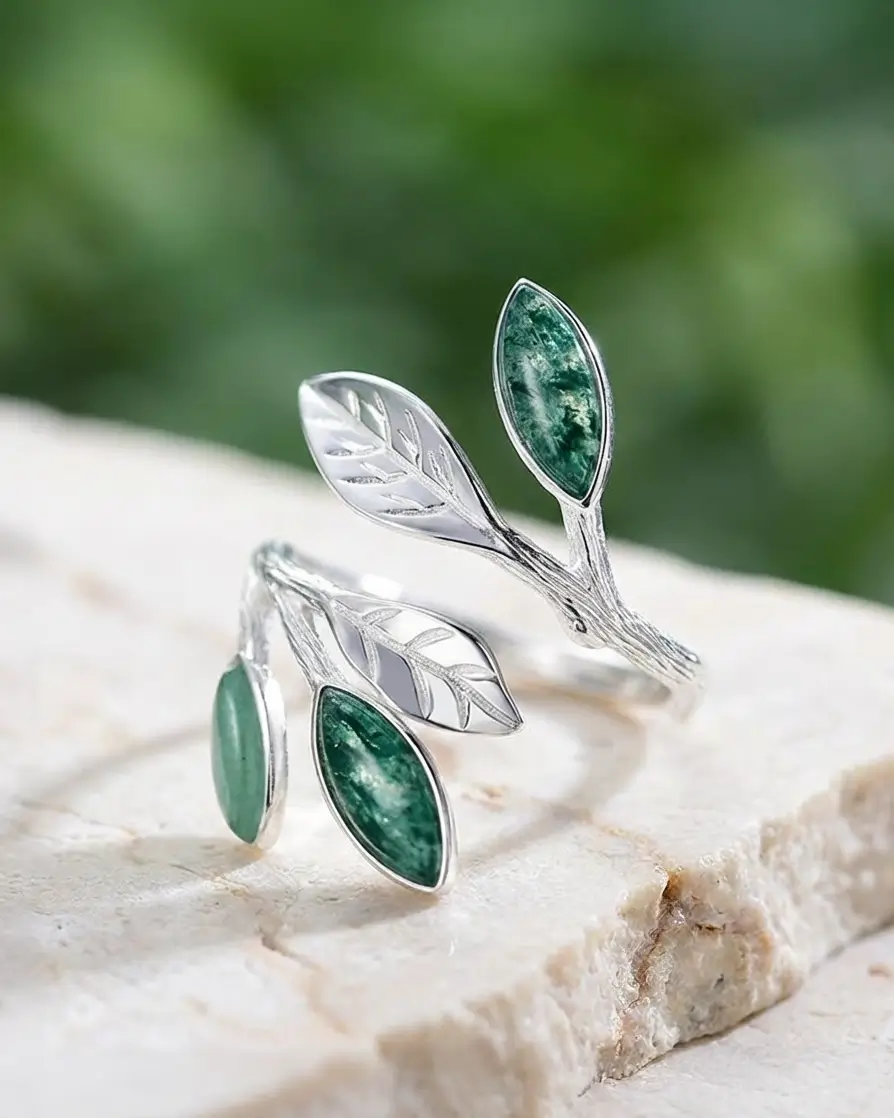 Bague feuillage en argent 925 sertie d’aventurine verte, posée sur pierre claire avec arrière-plan végétal flouté.