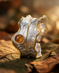 Bague feuille en argent 925 avec pierre naturelle tourmaline orange, mise en scène sur écorce et feuillage dans une ambiance végétale.