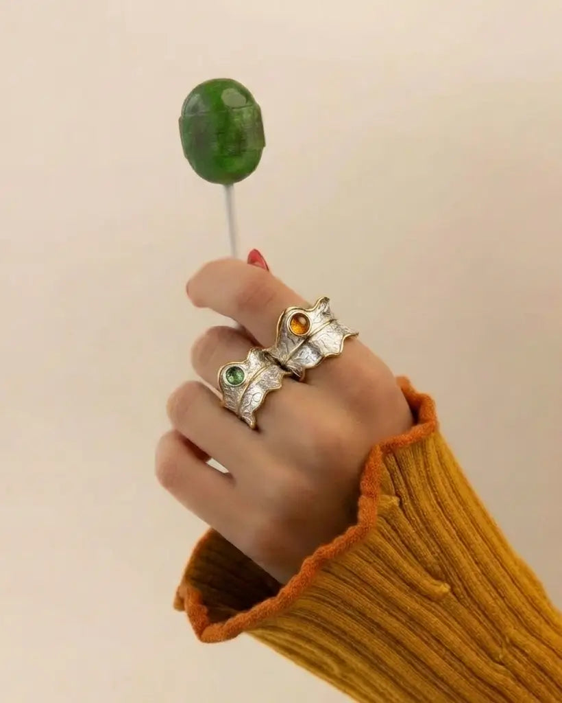Bagues feuille argent 925 sertie d’une tourmaline naturelle verte et orange portées à la main dans une mise en scène lifestyle douce et naturelle.