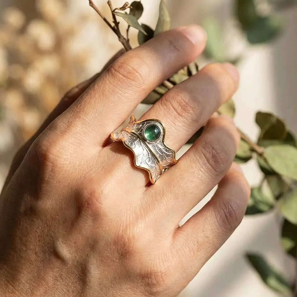 Bague feuille argent 925 et pierre naturelle tourmaline portée à la main, avec feuillage flouté en arrière-plan.