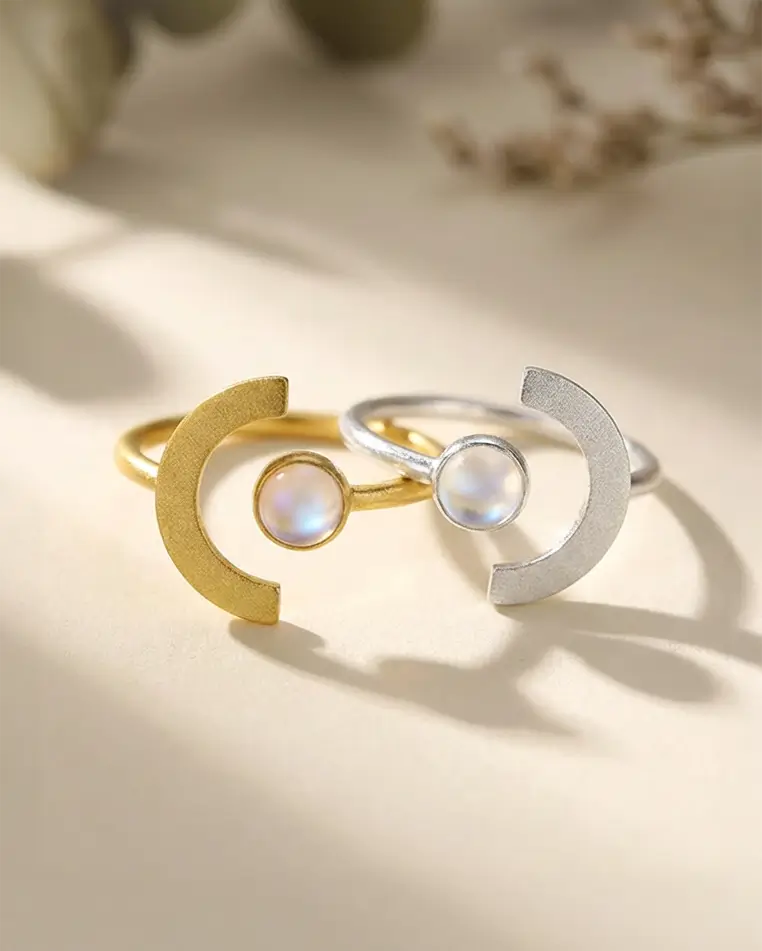 Duo de bagues Lune de Terre en argent 925 et émail glacé, finition dorée et argentée, posées dans une lumière douce et naturelle.