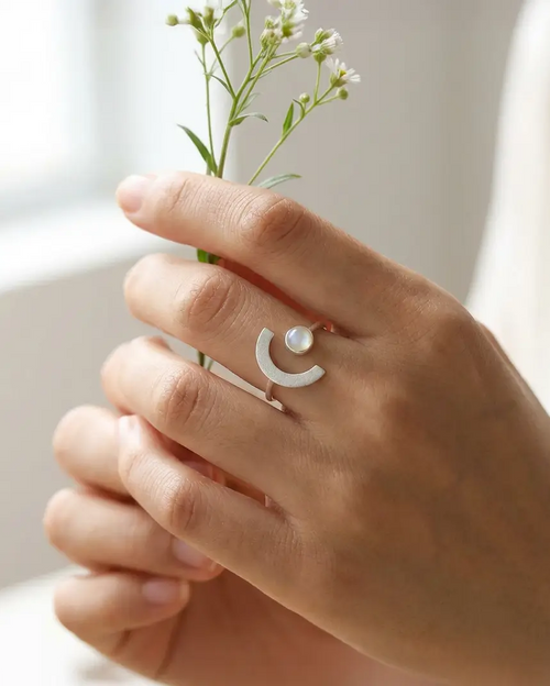 Bague Lune de Terre en argent 925 et émail glacé portée à la main, tenant une fleur sauvage, ambiance poétique et naturelle.