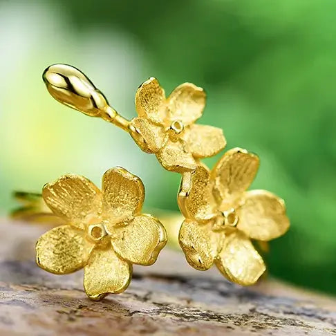 Gros plan sur les trois fleurs sculptées de la bague en argent 925 doreé, texture florale raffinée.