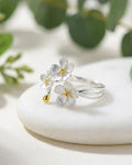 Bague trois fleurs ajustable en argent 925, bouquet floral délicat posé sur fond clair minimaliste.