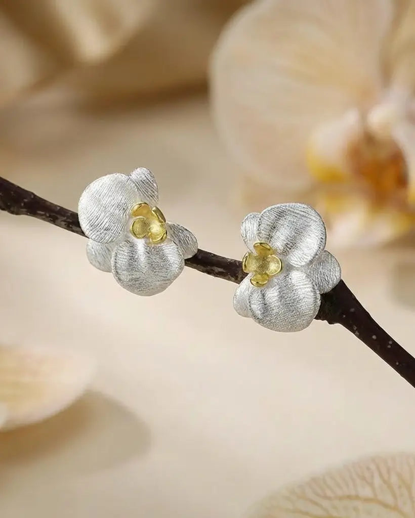 Boucles d’oreilles orchidées en argent 925 avec finition dorée, mises en scène sur une branche aux fleurs délicates.