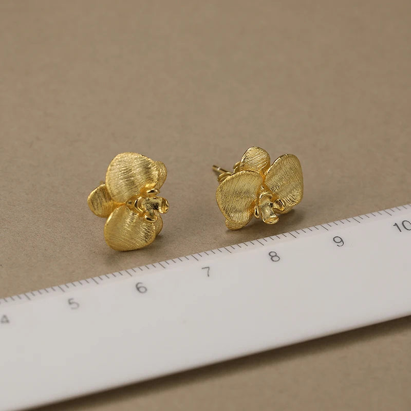 Boucles d’oreilles orchidées en argent 925 avec finition dorée présentées avec une règle pour visualiser les dimensions.