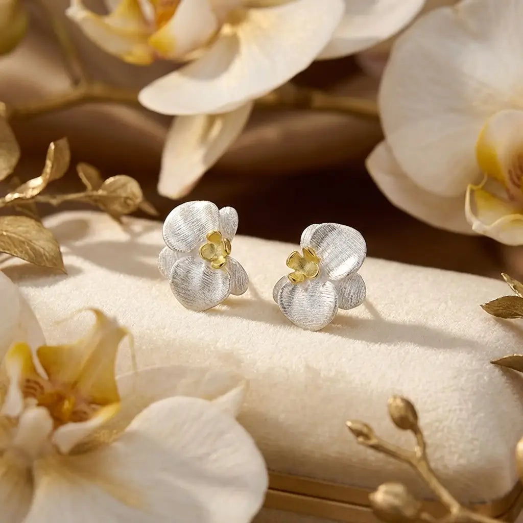 Boucles d’oreilles orchidées en argent 925 posées sur une surface claire, design floral délicat et lumineux.