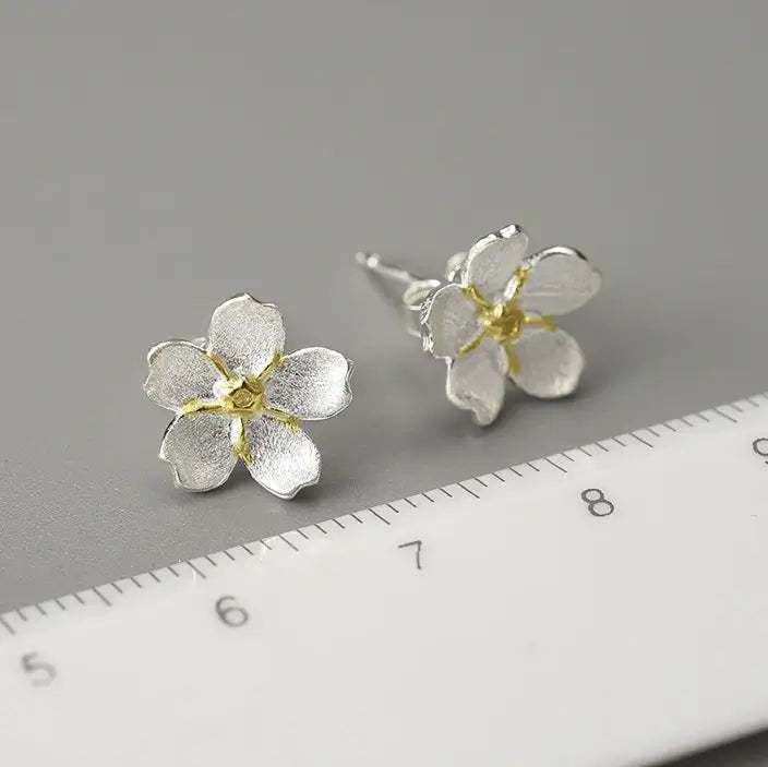 Boucles d’oreilles pâquerette en argent avec cœur doré et émail blanc montrant les dimensions précises sur une règle.