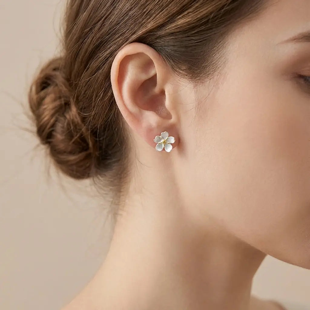 Boucles d’oreilles pâquerette en argent avec cœur doré et émail blanc portées de profil, rendu délicat et raffiné.