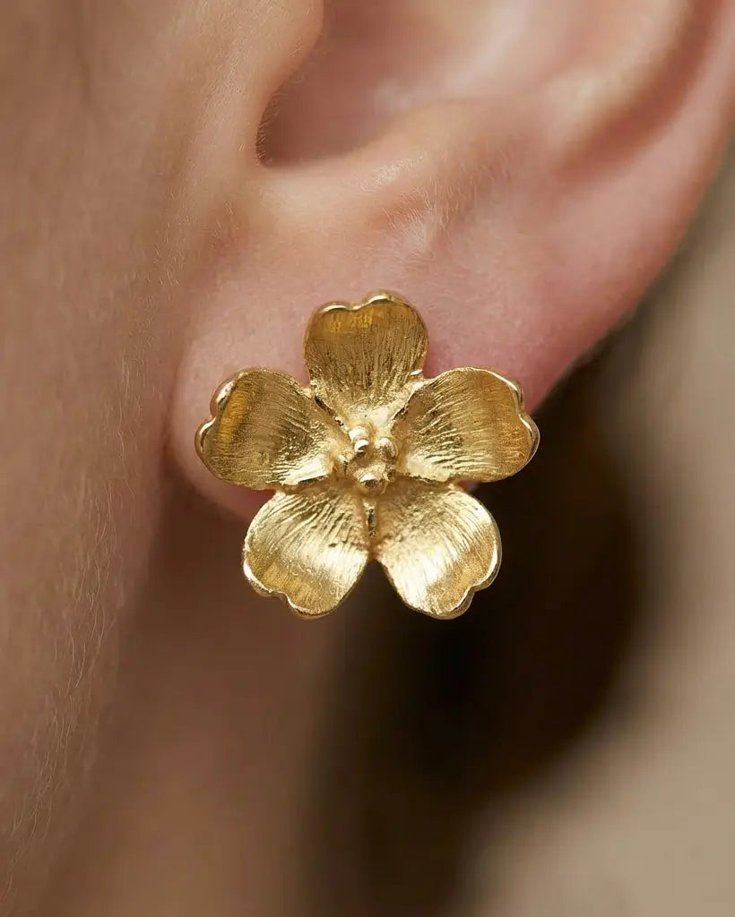 Gros plan sur des boucles d’oreilles pâquerette en argent doré et émail blanc, mettant en valeur la texture dorée et les pétales.