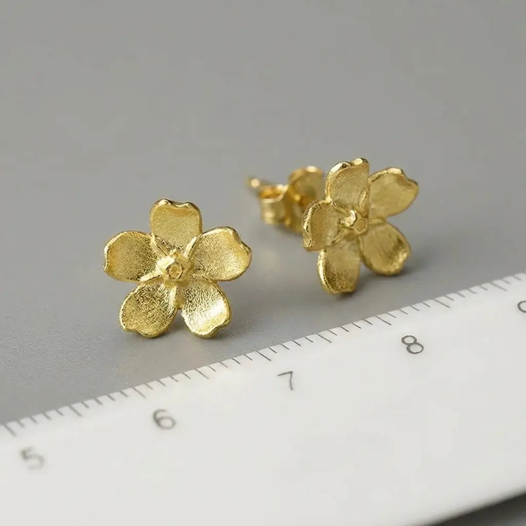 Boucles d’oreilles pâquerette en argent doré et émail blanc présentées avec une règle pour visualiser les dimensions.