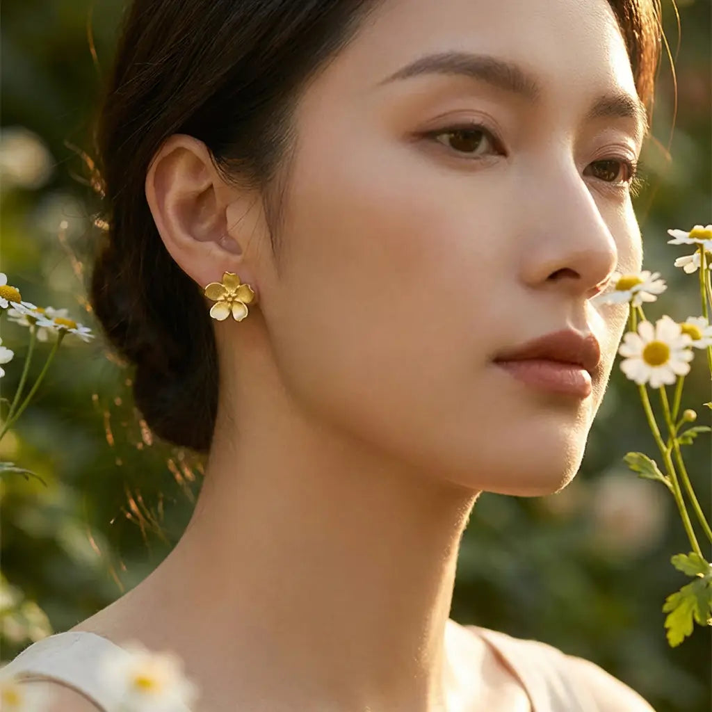 Boucles d’oreilles pâquerette en argent doré et émail blanc portées par une femme, style lumineux et naturel en extérieur.