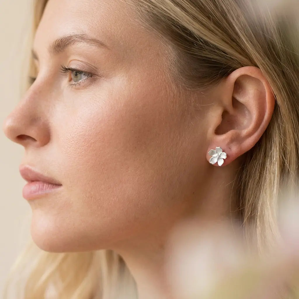 Boucles d’oreilles pâquerette en argent et émail blanc portées de profil, rendu discret et raffiné.