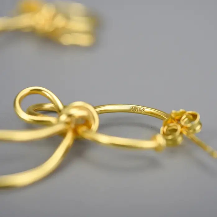 Vue macro des boucles d’oreilles volutes en argent 925 avec finition or, détails du métal et courbes organiques.