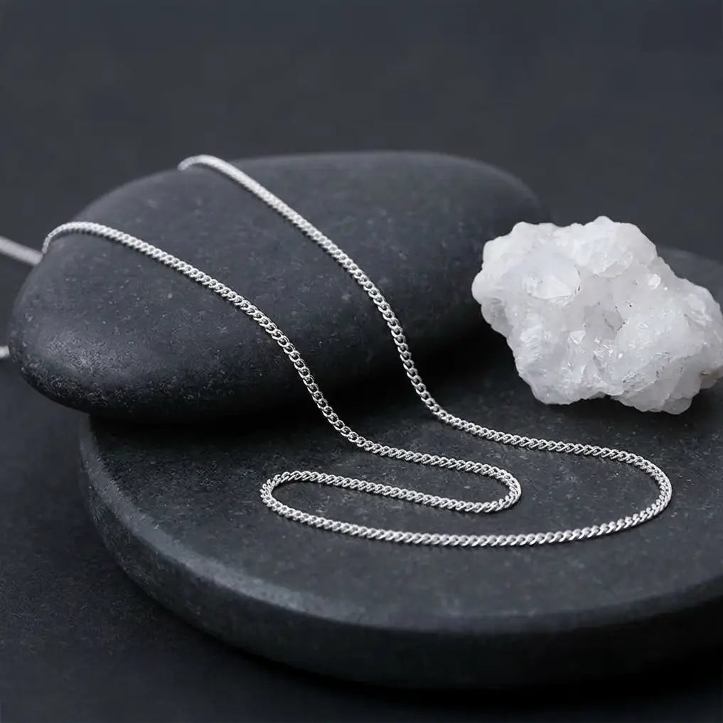 Chaîne minimaliste en argent 925 posée sur des galets et un cristal, ambiance minérale.