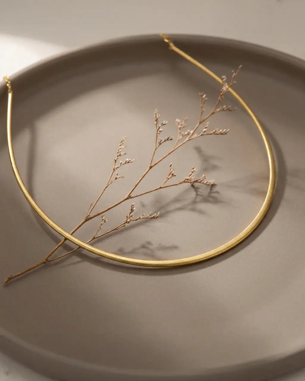 Chaîne torque rigide en argent 925 posée sur une mise en scène minérale aux accents dorés