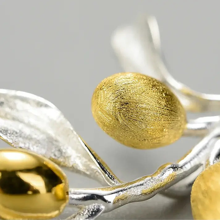Gros plan sur le collier branche d’olivier en argent et doré, détail des feuilles sculptées et olives dorées.