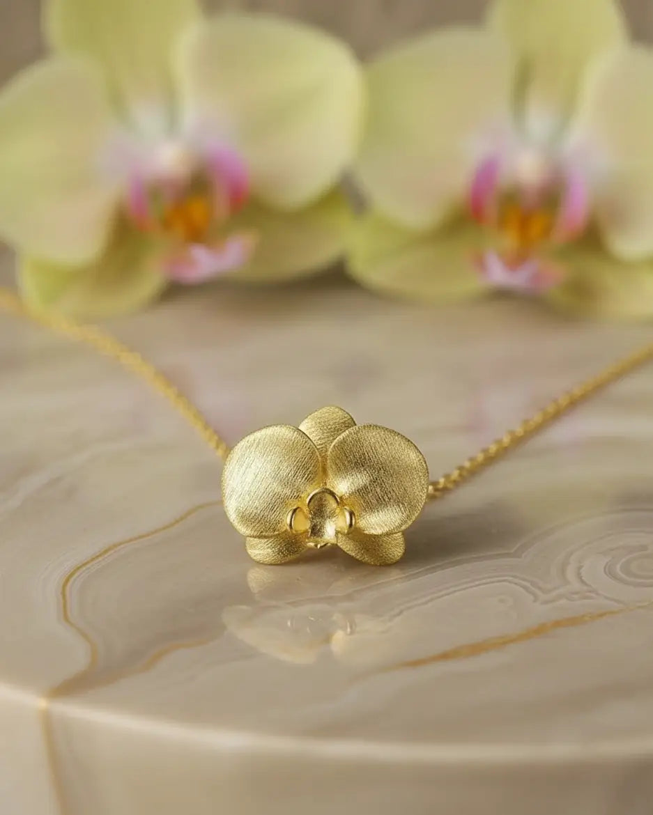 Collier orchidée en argent 925 avec finition or, posé sur un fond clair aux inspirations florales, ambiance douce et élégante.