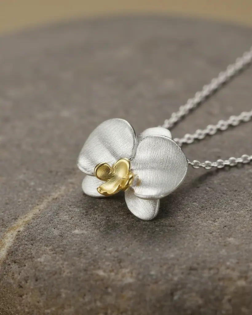Gros plan sur le pendentif orchidée en argent 925 avec finition or, mettant en valeur la texture des pétales.