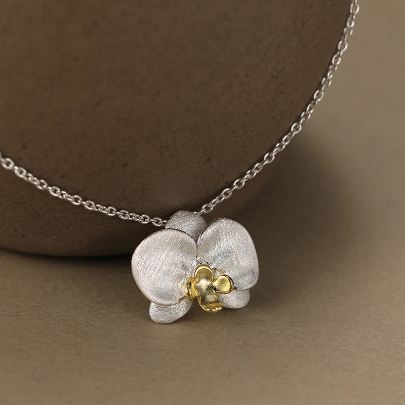 Collier orchidée en argent 925 avec finition or porté sur fond neutre, mettant en valeur le pendentif floral.