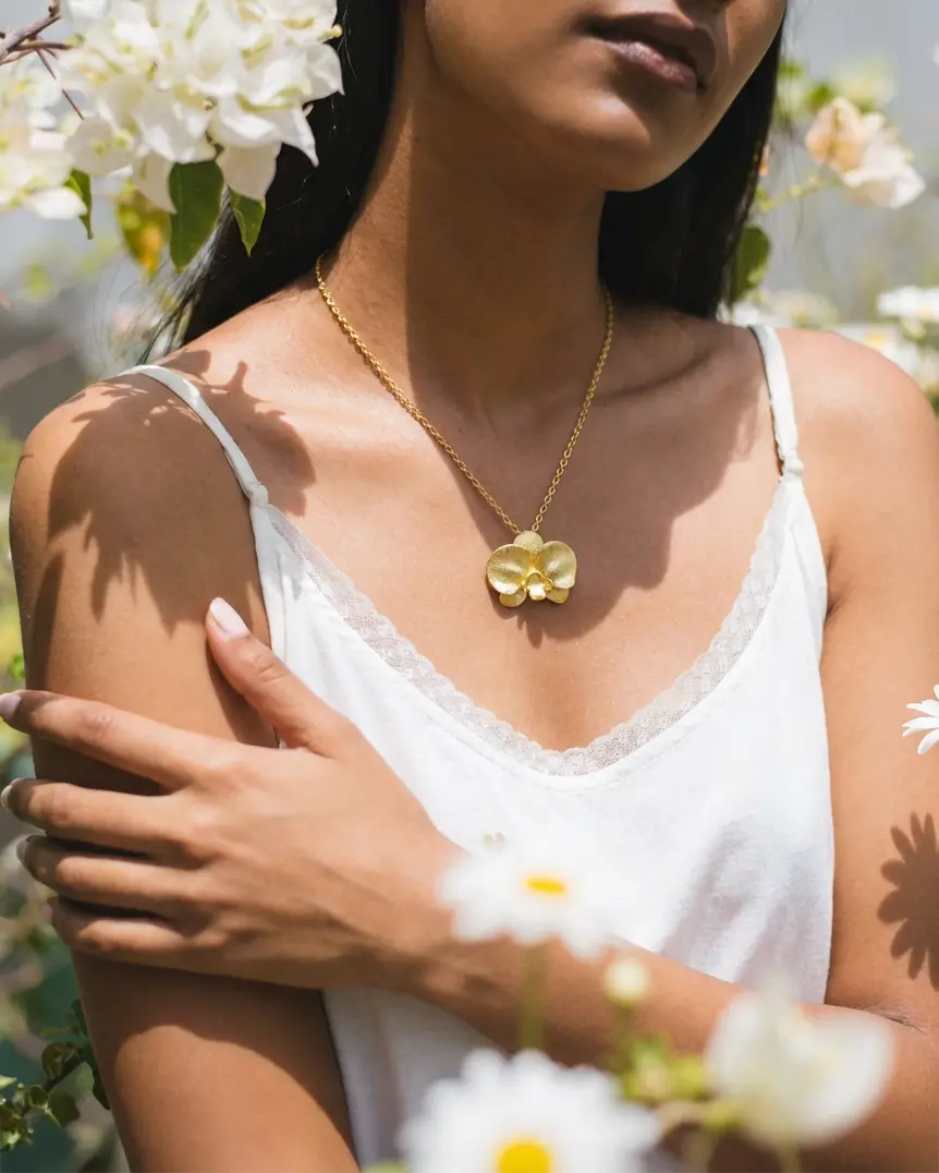 Collier orchidée en argent 925 avec finition or porté par une femme, style naturel et délicat en extérieur.