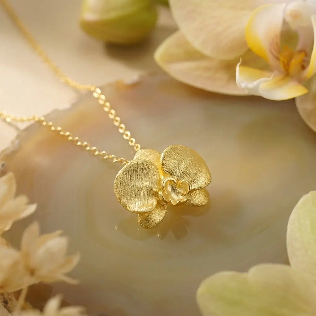 Collier orchidée en argent 925 avec finition or posé sur une surface claire, rendu lumineux et raffiné.