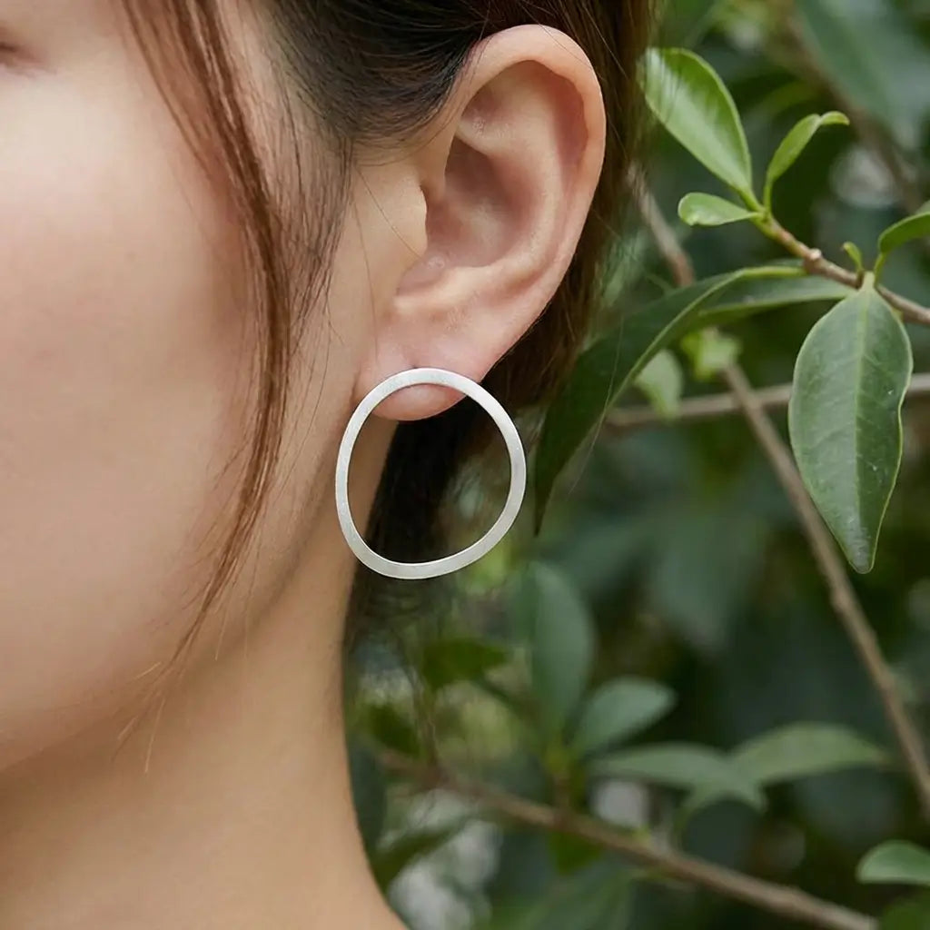 Créoles organiques en argent 925 portées à l’oreille, forme arrondie et finition lisse.