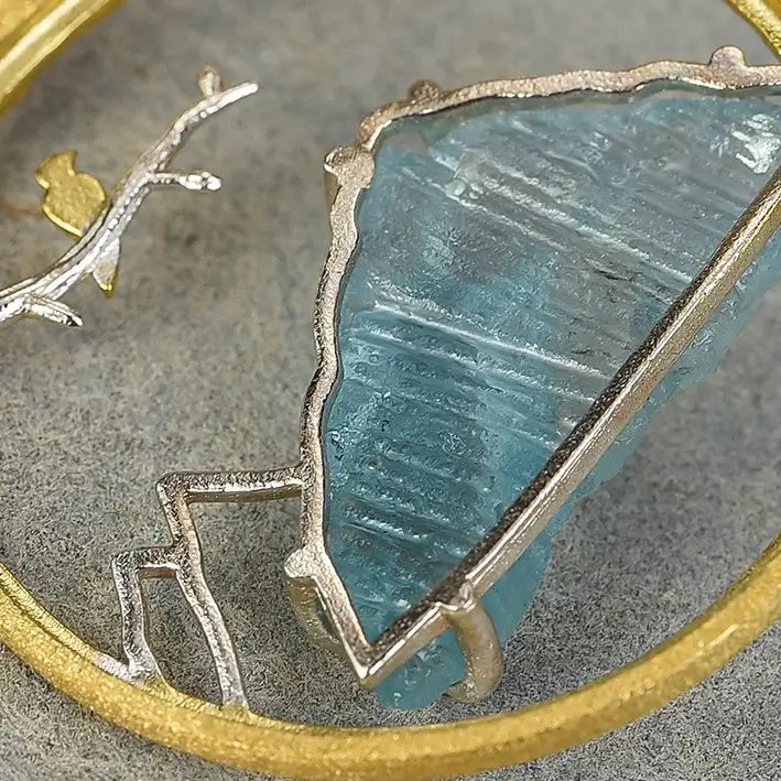 Gros plan sur le Médaillon Envol du Sommet en argent et or, montrant la pierre brute bleutée et la monture travaillée.