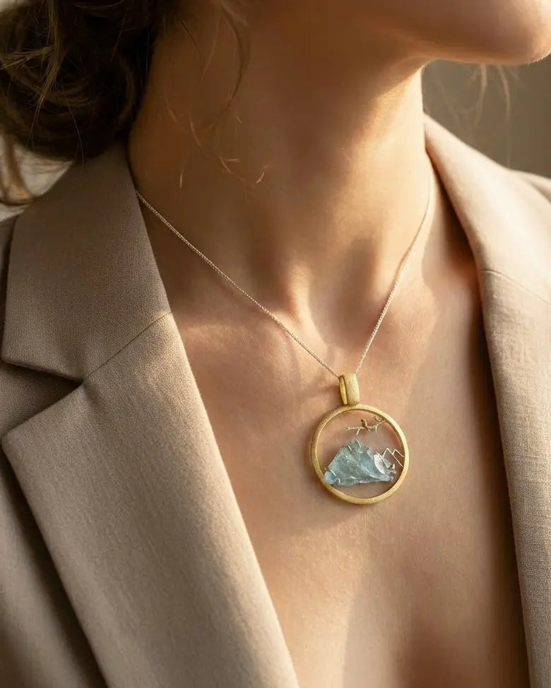 Médaillon Envol du Sommet en argent et or porté par une femme, bijou circulaire avec pierre brute bleue au centre.