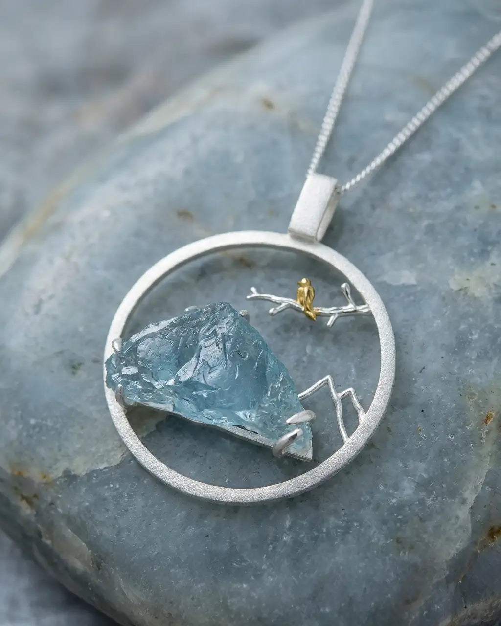 Médaillon Envol du Sommet en argent et or avec pierre brute bleutée, présenté à plat sur une surface minérale.