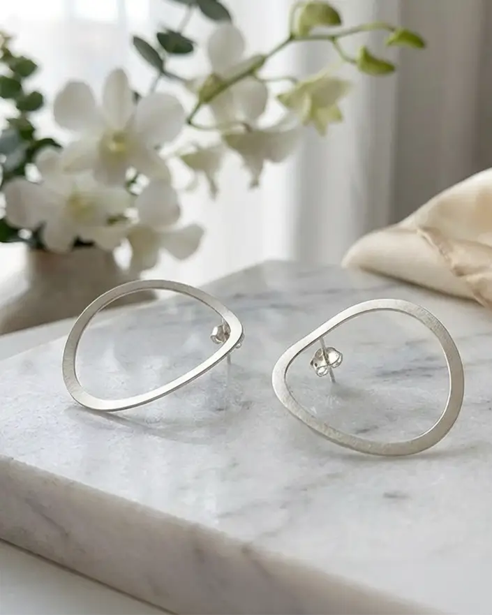 Créoles organiques en argent 925 posées sur une surface claire, design circulaire aux lignes douces.